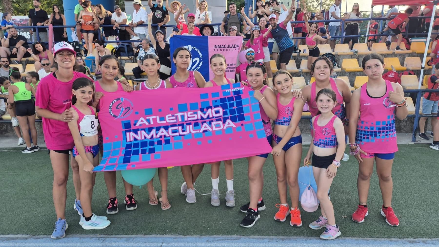 Atletas del club con la equipación rosa y la pancarta Atletismo Inmaculada